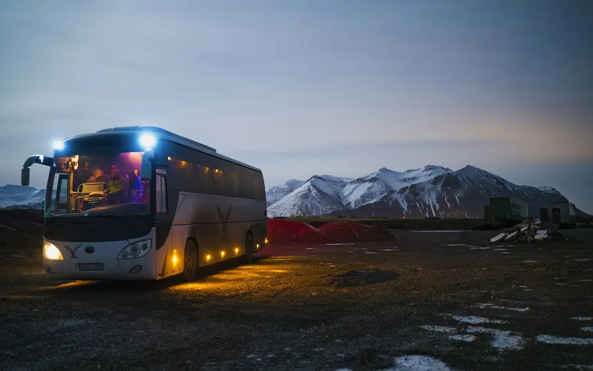Tourism & Tours Tour coach parked at dusk with snow-capped mountains behind it